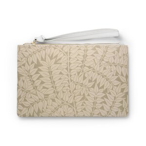 Puede incluir: Una cartera de mano beige con una cremallera blanca y una correa blanca. La cartera tiene un patrón de hojas.