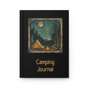 May include: A black journal with a camping scene illustration. The illustration features a yellow tent, campfire, and a full moon in a forest setting. The words "Camping Journal" are printed in gold.