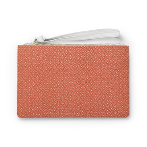 May include: A coral-colored clutch with a repeating pattern of small white dots and a white wrist strap. The clutch has a gold-colored zipper and a rectangular shape, suitable for carrying essentials.