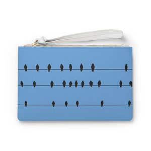 Puede incluir: Un bolso de mano azul claro con una cremallera y una correa blancas. El bolso tiene un diseño de pájaros negros en silueta sobre un alambre.