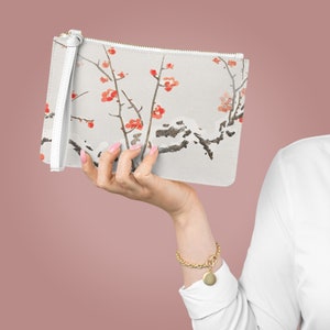 Puede incluir: Un bolso de mano blanco con un diseño floral que presenta ramas delicadas con flores rojas. El bolso tiene una correa blanca y un cierre de cremallera.