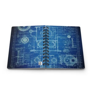 May include: Open spiral-bound notebook with a blueprint design. The pages display a detailed technical drawing in white against a blue background. The notebook is open, revealing the intricate design.