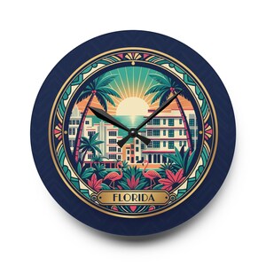 May include: Round wall clock with a navy blue face and a decorative Florida design. The design features palm trees, buildings, flamingos, and the word "FLORIDA" in a gold frame. The clock hands are black.