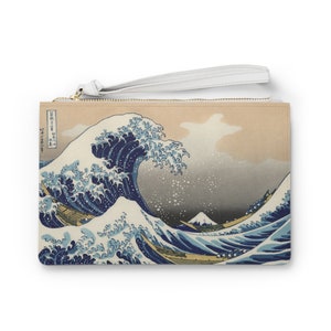 Puede incluir: Un clutch de lona beige con una cremallera blanca y una correa de muñeca blanca. La parte delantera del clutch presenta una impresión de "La Gran Ola de Kanagawa" de Katsushika Hokusai, una famosa estampa japonesa en madera que representa una gran ola con el monte Fuji en el fondo.