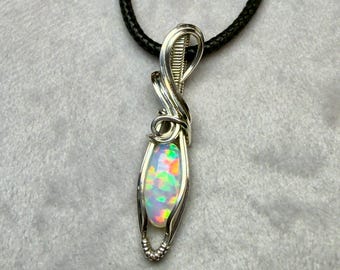 May include: A handcrafted pendant necklace featuring a vibrant opal gemstone encased in a silver wire wrap. The opal displays a spectrum of colors, including green, yellow, and orange. The pendant hangs from a black cord, creating a striking contrast.