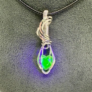 May include: A silver wire wrapped pendant with a green heart-shaped glass bead. The pendant is hanging from a black cord.
