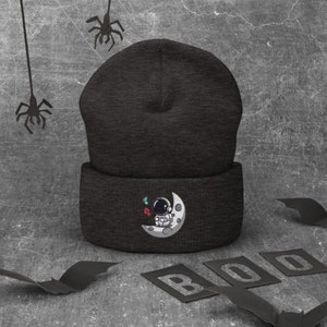 Ternura cósmica desatada: ¡Adorable astronauta con un gorro lunar de dibujos animados para entusiastas del espacio!