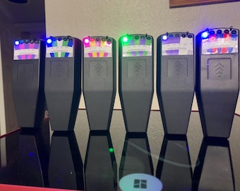 Könnte beinhalten: Sechs schwarze Geräte mit farbigen Displays und beleuchteten Lichtern. Jedes Gerät hat eine rechteckige Form mit einem Pfeildesign. Die Geräte sind in einer Reihe auf einer reflektierenden Oberfläche angeordnet. Der Text "MARCAUSSINO" ist auf den Displays sichtbar.