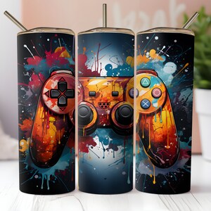 May include: Three stainless steel tumblers with a colourful paint splatter design and a video game controller graphic. The tumblers are black and have a straw.