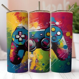 May include: Three colorful stainless steel tumblers with a graphic of a video game controller. The tumblers have a splatter paint design with yellow, red, blue, green, and purple paint splatters.