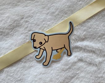 May include: A tan puppy sticker with a black outline and light blue background. The puppy is urinating, with a yellow stream. The sticker is on a white, fluffy surface with a yellow ribbon.