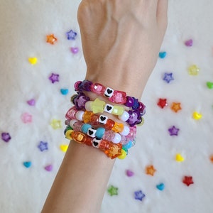 May include: A stack of colorful beaded bracelets with black heart charms. The bracelets are made of different colored beads, including pink, purple, yellow, and orange. The bracelets are stacked on a person's wrist.