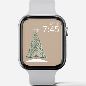 May include: A white Apple Watch with a brown background featuring a green Christmas tree with a white star on top. The time is 7:45 and the date is SAT 13.