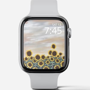May include: A silver Apple Watch with a white band displays a sunflower field with a cloudy sky and the time 7:45. The date is displayed as SAT 13.