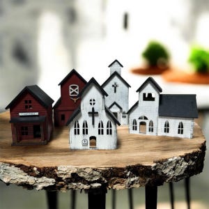Pode incluir: Uma coleção de cinco edifícios de madeira em miniatura, incluindo uma casa vermelha, um celeiro vermelho e três igrejas brancas com telhados pretos. As estruturas apresentam recortes detalhados para janelas e portas, com uma cruz numa igreja.