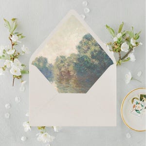 May include: A white envelope with a landscape painting inside, featuring trees and water in shades of green, blue, and brown. The envelope is surrounded by white flowers and petals, with a small dish and stamps in the corner.