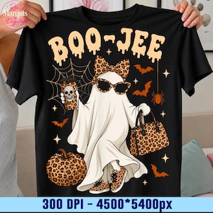 May include: A black t-shirt featuring a graphic of a ghost wearing leopard print sunglasses, a matching bow, and sneakers. The ghost holds a leopard print cup with a skull and a leopard print handbag. A pumpkin, bats, and spiderwebs surround it.