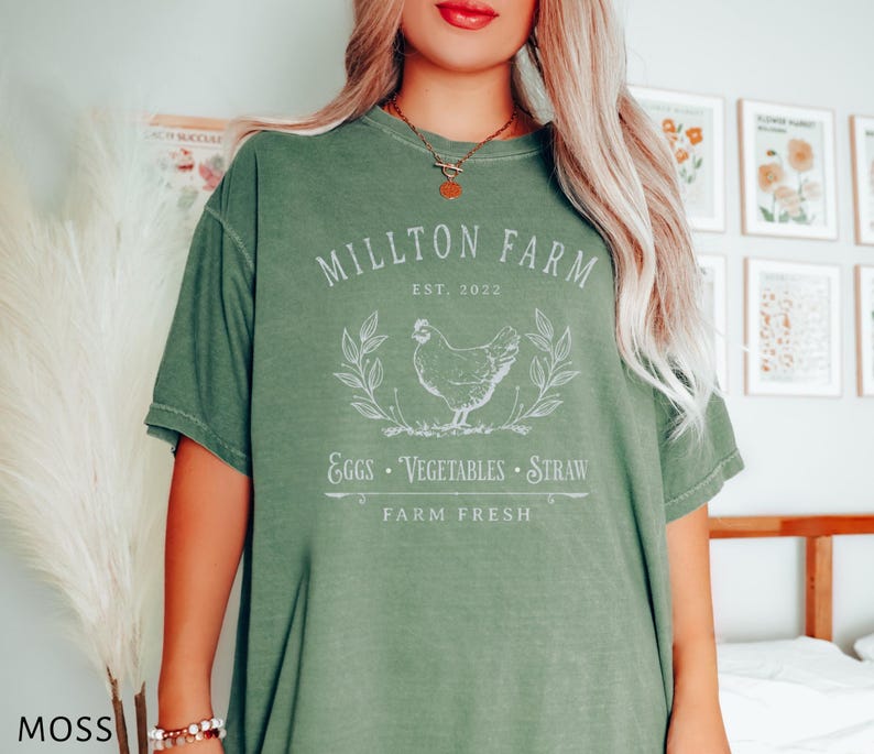 Puede incluir: Una camiseta verde con un dise&ntilde;o gr&aacute;fico blanco que dice "Millton Farm Est. 2022 Eggs - Vegetables - Straw Farm Fresh". El gr&aacute;fico tambi&eacute;n incluye un dibujo blanco de una gallina.