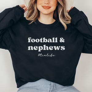 May include: Black sweatshirt with the text "football & nephews #tialife" in white.