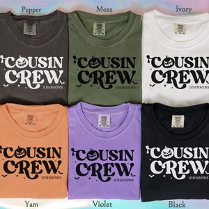 May include: Six t-shirts in various colors: pepper, moss, ivory, yam, violet, and black. Each shirt features the text "COUSIN CREW" with a jack-o'-lantern and bats, and the name "JOHNSONS". The shirts are folded and displayed.