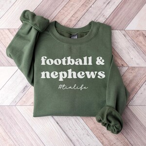 May include: A green sweatshirt with the text "football & nephews #tialife" in white.