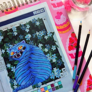May include: A spiral-bound sketchbook with a pink cover featuring a whimsical cake design. The open page displays a vibrant illustration of a blue tiger within a computer window frame, surrounded by blue flowers. Colored pencils and a glass of water are also present.