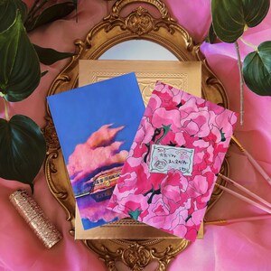 May include: Two postcards with a pink floral design and a blue sky with a pink cloud and a train reflecting in water. The text on the floral postcard says "石膏♡" and "永遠のあなたへ".