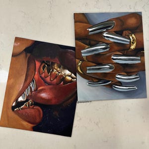 Op de afbeelding: Twee kunstdrukken. E&eacute;n toont een close-up van een mond met gouden tanden en rode lippen. De andere toont handen met zilveren chromen nagels en gouden ringen. De prints liggen op een wit oppervlak.
