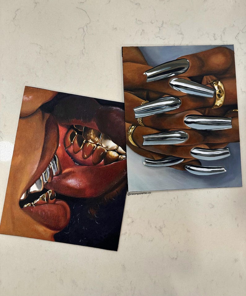 Op de afbeelding: Twee kunstdrukken. E&eacute;n toont een close-up van een mond met gouden tanden en rode lippen. De andere toont handen met zilveren chromen nagels en gouden ringen. De prints liggen op een wit oppervlak.