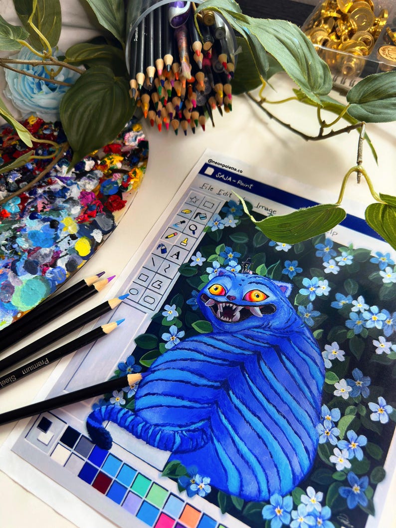 May include: An artistic still life featuring colored pencils, a paint palette, and a drawing of a blue cat with a menacing expression. The drawing is surrounded by blue flowers. The text "SAJA - Paint" is visible.
