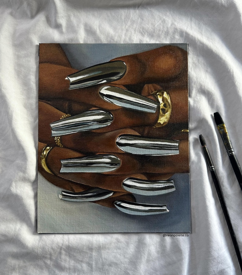 Op de afbeelding: Een schilderij van handen met lange, chroomkleurige nagels en gouden ringen. Het kunstwerk toont een close-up van de handen, waarbij de nagels het licht reflecteren. De achtergrond is een zachte, neutrale kleur en de handtekening van de kunstenaar is zichtbaar.