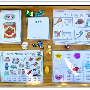 May include: A set of educational speech therapy cards and game boards featuring minimal pairs, I Spy activities, and word lists. The cards include illustrations of objects like a can, key, and cup, alongside small colorful plastic figurines and dice.