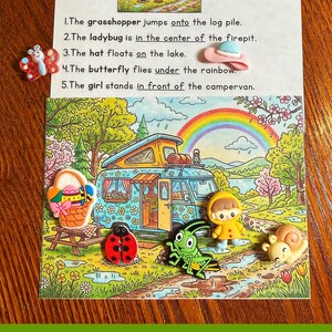 May include: A white educational card titled Ms. Melody's Miniatures featuring five numbered sentences about prepositions. The card includes a colourful illustration of a campervan, a rainbow, and five small plastic character buttons: a butterfly, a ladybug, a grasshopper, a child in a yellow raincoat, and a snail.