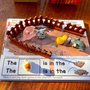 May include: A children's educational toy set with miniature farm animals, such as a pig, duck, and elephant, inside a brown wooden fence. The set includes a printed card with the text "Ms. Melody's Miniatures".