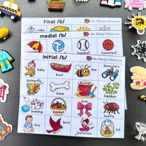 Puede incluir: Tres tablas fonéticas educativas etiquetadas como final /b/, medial /b/ e initial /b/ de Ms. Melody's Miniatures, rodeadas de varios pequeños dijes coloridos que incluyen un taxi, un cangrejo, una bombilla, una telaraña, un oso y un bebé.