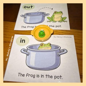 May include: Educational image featuring a green frog toy and two illustrated scenes. One scene shows a frog outside a pot, labeled "out," and the other shows a frog inside a pot, labeled "in." The text reads "The frog is in the pot."