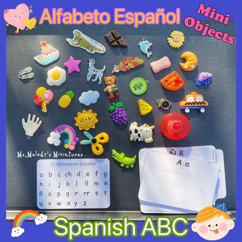 May include: A set of colorful miniature objects representing the Spanish alphabet. The objects include a pineapple, a watermelon, a cloud, a sun, a rainbow, a pair of scissors, a crocodile, a cow, a taxi, a feather, a dolphin, a bar of chocolate, a star, an egg, a dog, a teddy bear, a kiwi, a piece of cheese, a bunch of grapes, a hand, a balloon, a moon, a flower, and a heart. The set also includes a card with the Spanish alphabet printed on it.