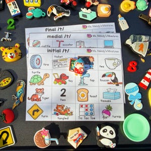 Puede incluir: Una colección de imanes coloridos y materiales educativos, incluyendo una hoja de trabajo con palabras como "tire" y "turtle". Varios imanes temáticos, como un tigre, un tucán y un panda, están dispersos alrededor de la hoja de trabajo.