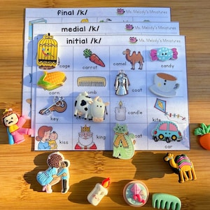 May include: A selection of colourful miniature figurines and flashcards for educational use. The flashcards are labelled with the text "final /k/", "medial /k/", and "initial /k/". The figurines include a cage, carrot, camel, candy, corn, comb, coat, candle, key, cow, kite, cat, car, and king.