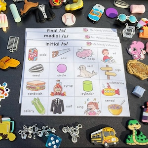 Könnte beinhalten: Eine Sammlung von Miniatur-Anhängern und ein Arbeitsblatt. Das Arbeitsblatt zeigt Wörter, die mit dem Buchstaben "s" beginnen, wie "soda", "saw" und "soap". Die Anhänger umfassen einen Baseball, einen Schulbus und eine Schlange.