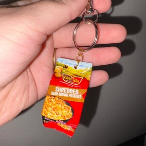 May include: A red and yellow Ore-Ida Shredded Hash Brown Potatoes keychain. The keychain is attached to a silver key ring.