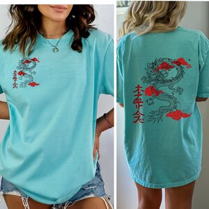 May include: A light blue t-shirt with a red and black dragon graphic and Japanese characters on the back. The front of the shirt has a smaller version of the dragon graphic and Japanese characters.