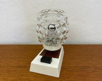 May include: A white and brown bedside lamp with a clear glass shade featuring a bubbled texture. The lamp has a black on/off switch.