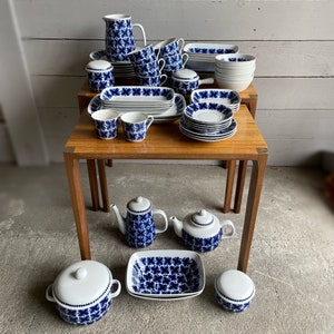 May include: A set of blue and white floral patterned ceramic dinnerware, including plates, bowls, cups, saucers, a teapot, a sugar bowl, and a creamer. The dishes are arranged on two wooden tables.