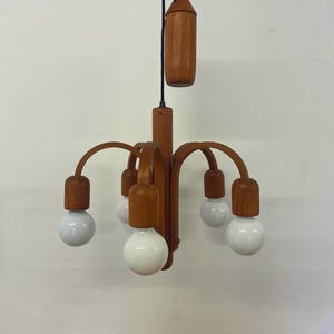 Puede incluir: Una lámpara de araña de madera de estilo moderno de mediados de siglo, con seis bombillas globo blancas. La lámpara tiene un acabado de madera natural y un cable de tracción. El diseño presenta brazos curvos y un soporte central.