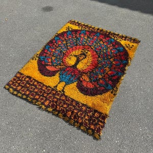 May include: A rectangular rug with a vibrant, abstract design. The rug features a yellow background with a central pattern of red, blue, and orange shapes. The border is a darker brown with a geometric pattern. The rug is approximately 36 inches long and 24 inches wide.