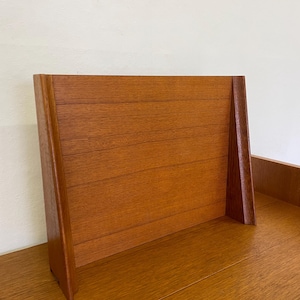 May include: A mid-century modern wooden headboard with a warm, reddish-brown finish. The headboard features a rectangular design with horizontal wooden slats and angled side supports. The wood grain is visible, adding texture and character to the piece.