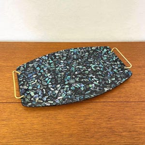 May include: Decorative serving tray with a black and iridescent mosaic pattern. The tray has a rectangular shape with rounded ends and gold-colored handles. The mosaic design features shades of black, teal, and blue.