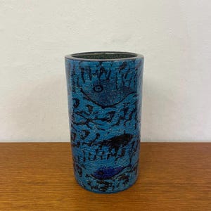 Puede incluir: Un jarrón de cerámica azul con un diseño abstracto en blanco y negro. El jarrón tiene una forma cilíndrica y una superficie texturizada.