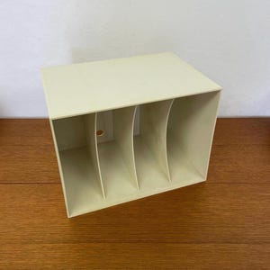 Puede incluir: Un revistero de plástico blanco con cuatro compartimentos. El revistero está vacío y se encuentra sobre una superficie de madera.